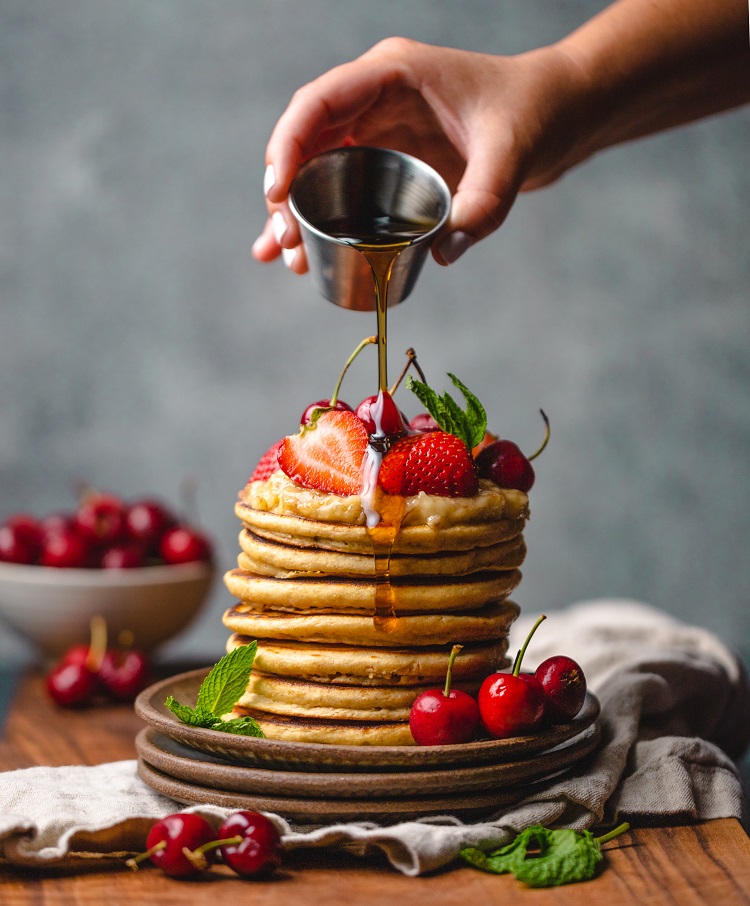 a stack of pancakes with fruit and dripping maple syrup