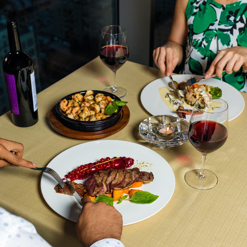 two people having dinner, one eating a red meat dish and the other having chicken with grenache wine