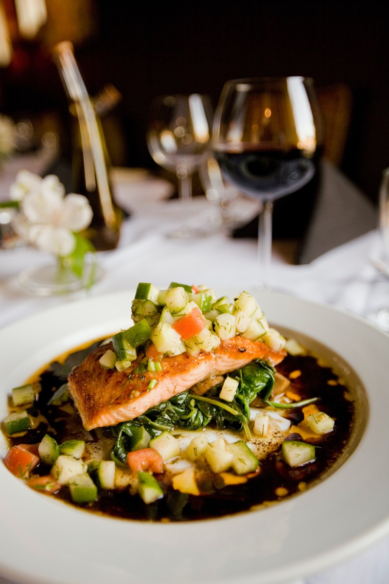 a salmon dish with fresh vegetables and spinach served with a glass of grenache wine