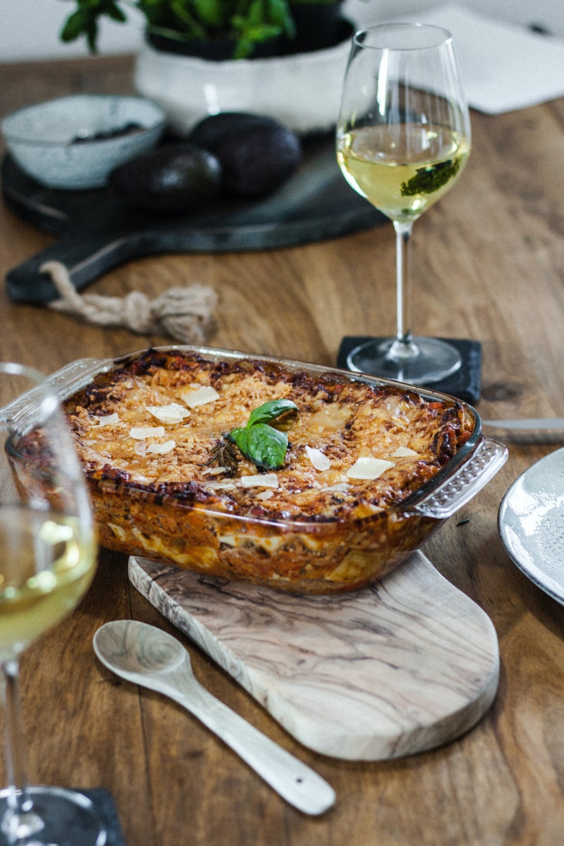 a casserole of lasagna next to a glass of white wine